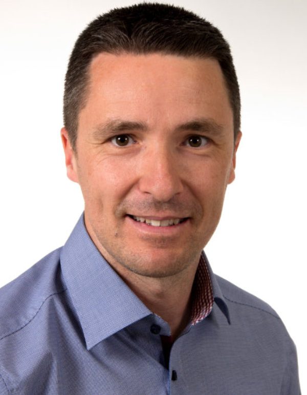 Porträt eines Mannes mit kurzen, dunklen Haaren in einem hellblauen Hemd.