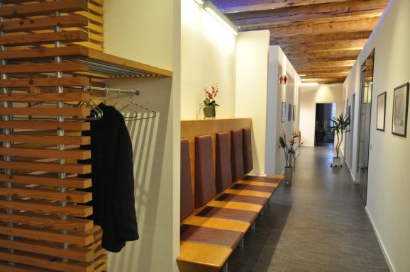 Hellbrauner Flur mit Holz-Paneelen, Sitzbänken und Pflanzen entlang der Wände.