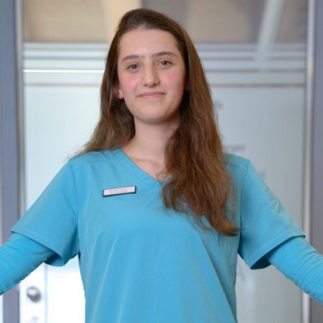 Eine junge Frau in einem hellblauen T-Shirt mit langen Haaren und lächelndem Gesicht.
