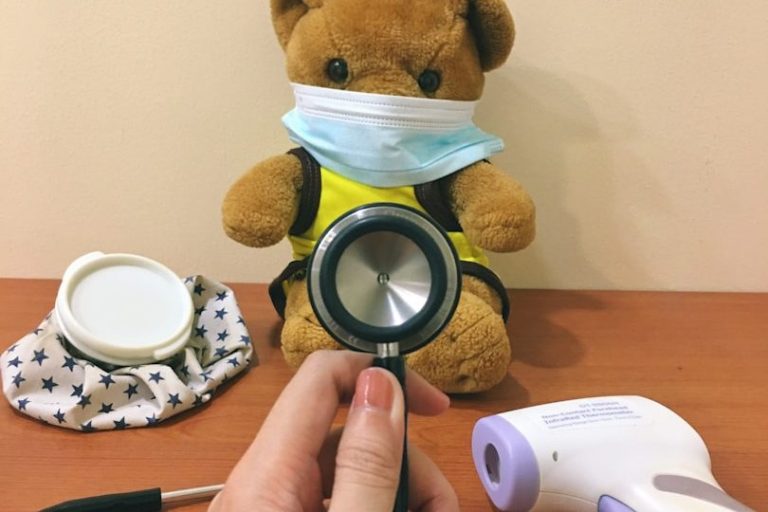 Ein Bär mit Mundschutz trägt eine gelbe Weste, während ein Stethoskop gehalten wird.