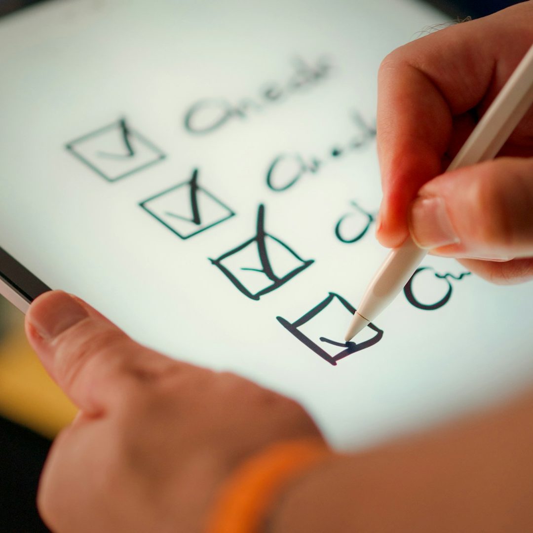 Hand, die mit einem Stift auf einem Tablet eine To-Do-Liste mit Häkchen bearbeitet.