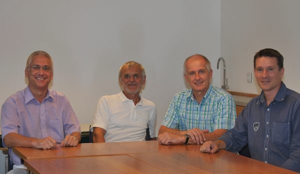 Vier Männer sitzen an einem Tisch und lächeln in die Kamera.