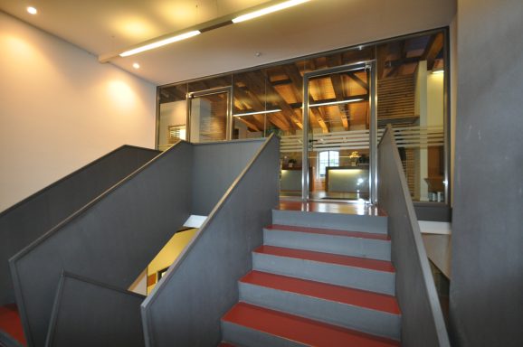 Treppenhaus mit Holzdecken, grauen Wänden und roten Stufen.