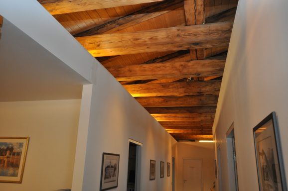 Ein heller Flur mit Holzdeckenbalken und gerahmten Bildern an den Wänden.
