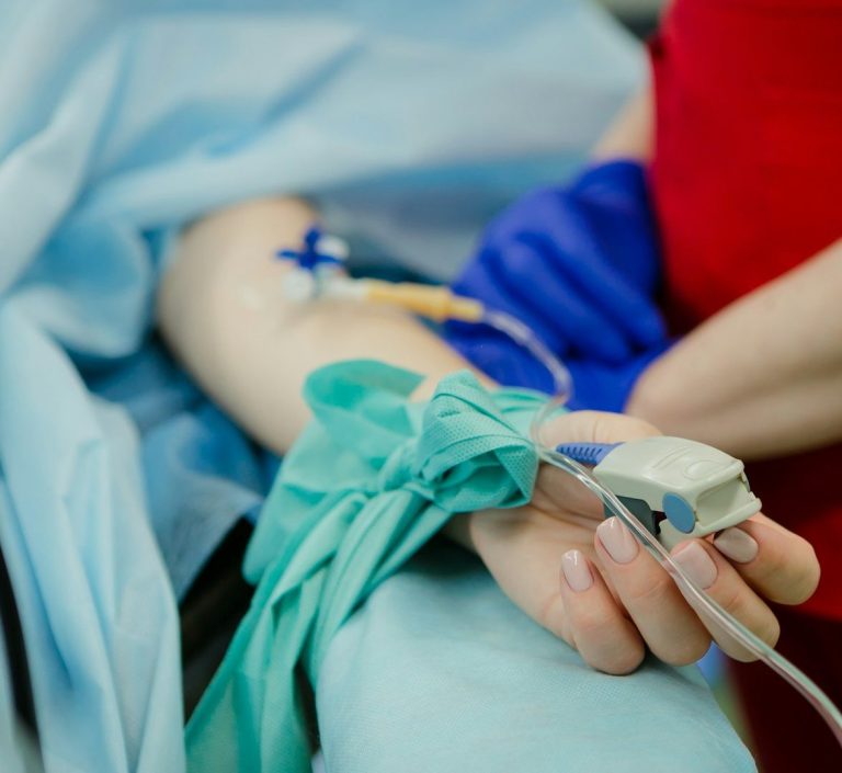 Hand mit IV-Katheter und Monitor an einem arm, in einem medizinischen Umfeld.