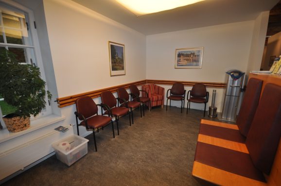 Leerer Warteraum mit roten Stühlen, einem Pflanze und einer Wasserstation.