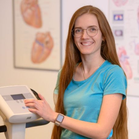 Junge Frau mit Brille und langen Haaren an einem Fitnessgerät in einem Labor.