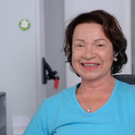 Frau mit kurzen, braunen Haaren und lächelndem Gesicht in einem Büro.