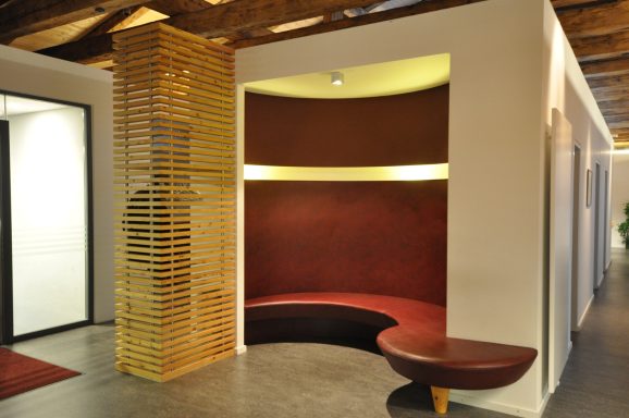 Moderne Empfangsarea mit gewellter, roter Bank und goldenem Sichtschutz.