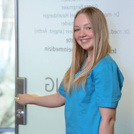 Junge Frau in blauer Kleidung, die eine Tür aufhält und lächelt.