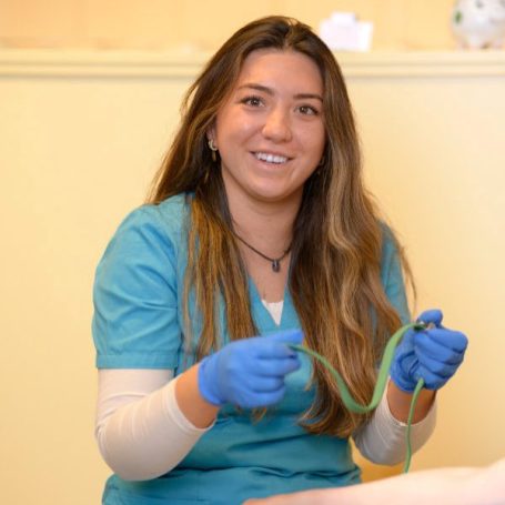 Frau in blauer Arbeitsbekleidung mit Handschuhen und einem Schlauch in der Hand.
