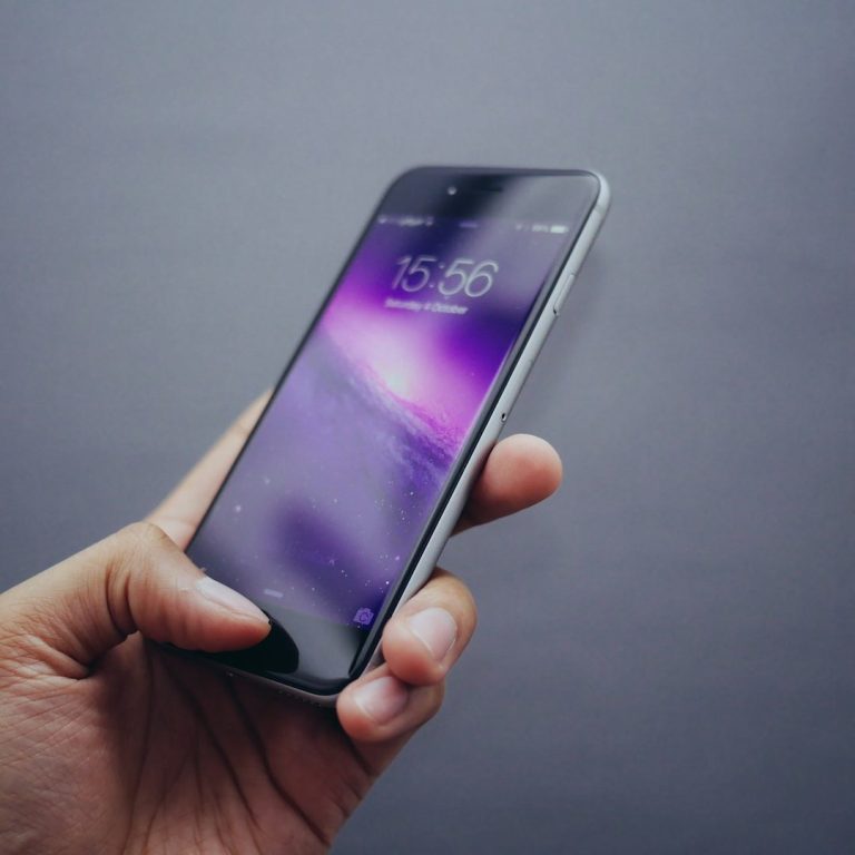 Hand hält ein Smartphone mit einem lila Hintergrund auf dem Bildschirm.