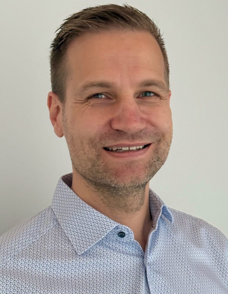 Mann mit kurzem, blondem Haar und leichtem Lächeln, trägt ein hellblaues Hemd.