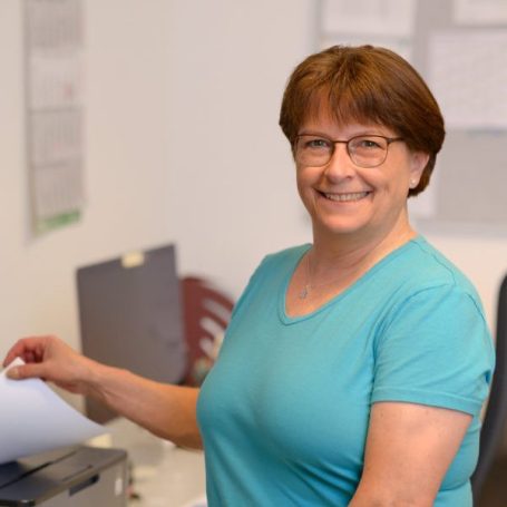 Frau in blauem Shirt druckt Unterlagen an einem Drucker in einem Büro.