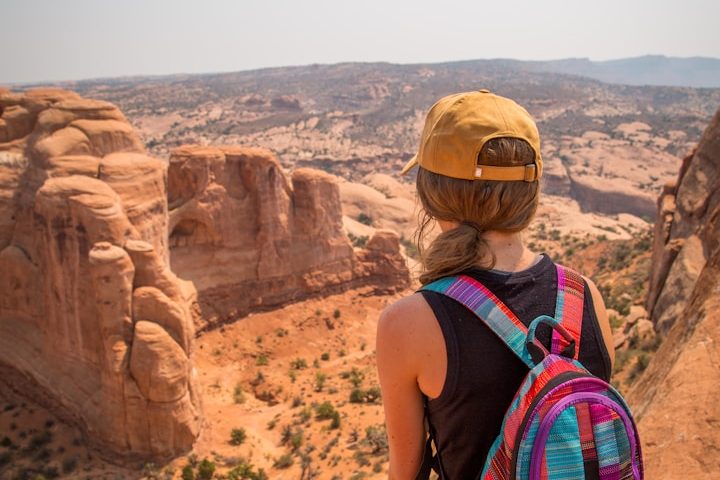 Frau mit Rucksack und gelber Cap blickt auf eine beeindruckende Felslandschaft.