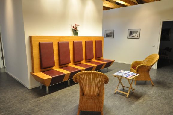 Wartebereich mit Holzbänken, einem Stuhl und einem Tisch mit Zeitschriften.